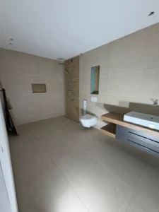 Modernes Badezimmer mit bodenebener Dusche, großformatigen Fliesen und Holzoptik-Akzentwand in Düsseldorf MK Innenausbau